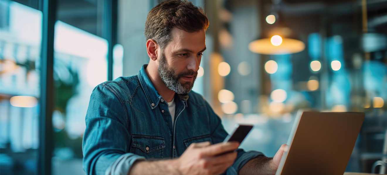 man sat at laptop with mobile device in hand