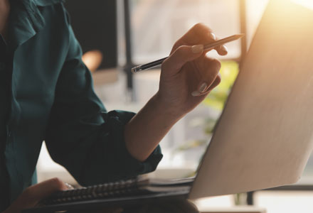 person pointing towards monitor with pen in hand