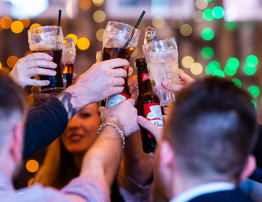 A group toasting with drinks. Pretty blurred fairy lights are in the background.