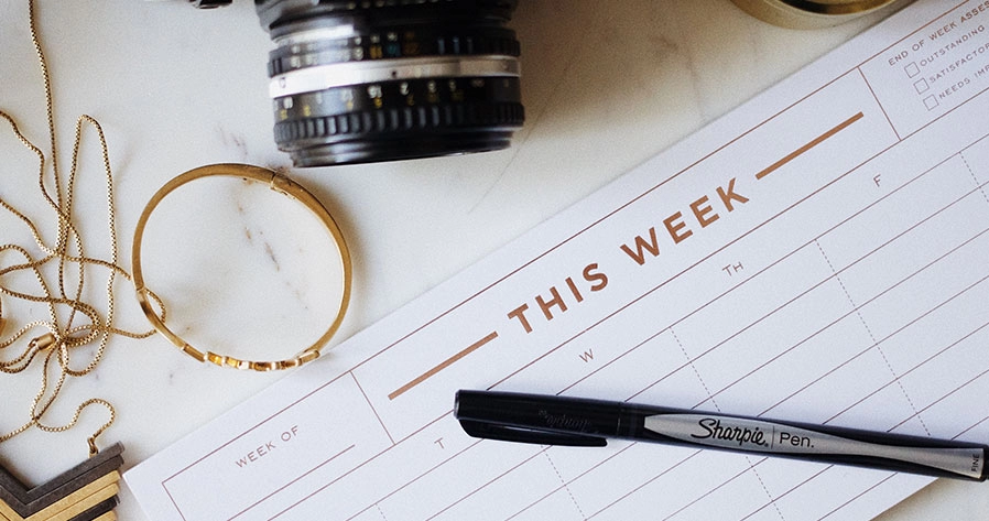 A stylish weekly planner with a pen resting on top.