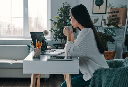 female sat at computer sipping a drink