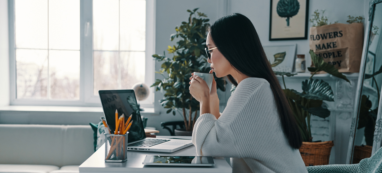 female sat at computer sipping a drink