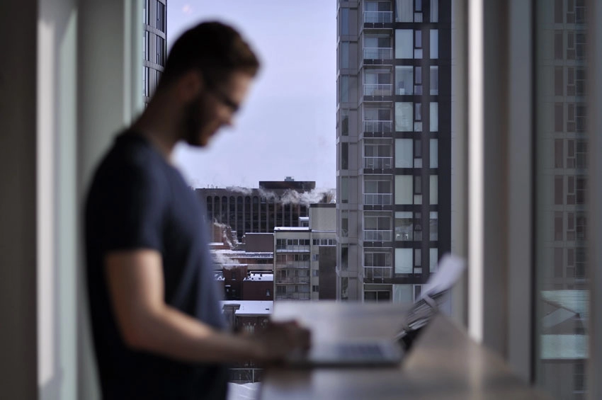 An out of focus shot of a man standing over a laptop, with a clear focus on the city buildings and skyscrapers in the background.