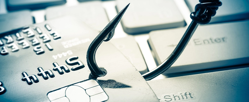 A closeup shot of a sharp pointed fishhook piercing a credit card on top of a keyboard. The fishhook is a dark contrast against the light washed out colours.