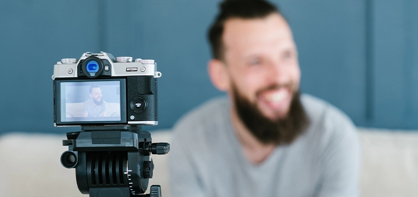 A camera screen with an in focus shot of the blurred man sat smiling in the background. He looks slightly away from the camera.