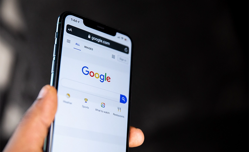 A hand holding a modern phone with the google homepage displayed.