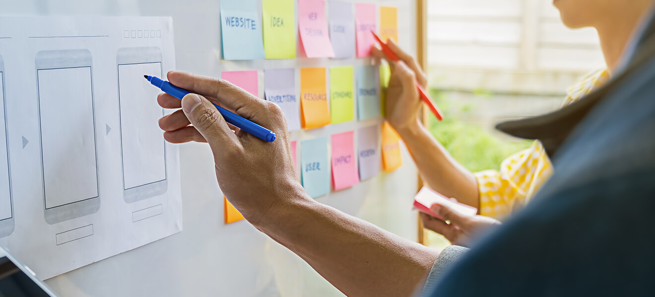 People drawing on a board with illustrations and sticky notes.