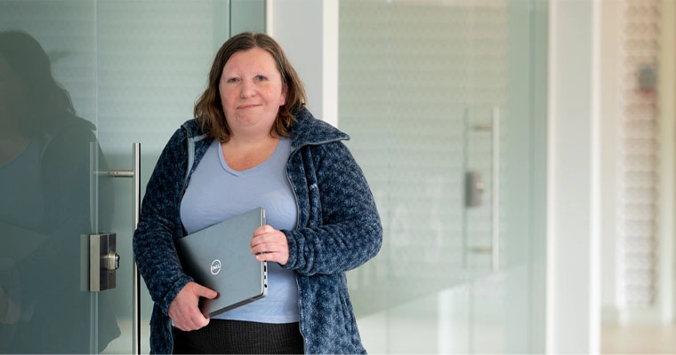 An accessibility tester standing and holding a laptop.