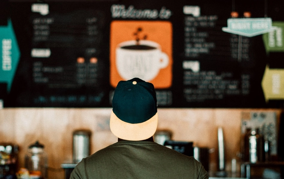 A confused customer stands in front of a large cafe menu.