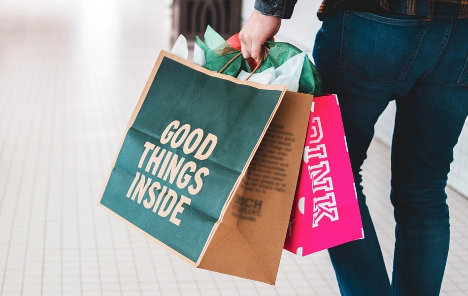 A person struggles to carry multiple shopping bags whilst one of the bags says 'good things inside'.