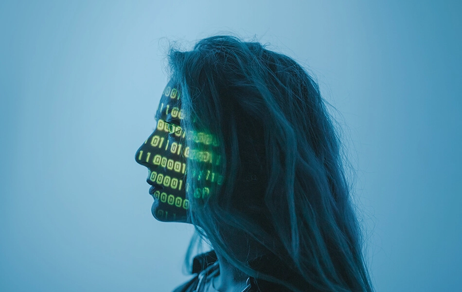 A human stares vacantly into the distance whilst green binary code is projected onto their face.