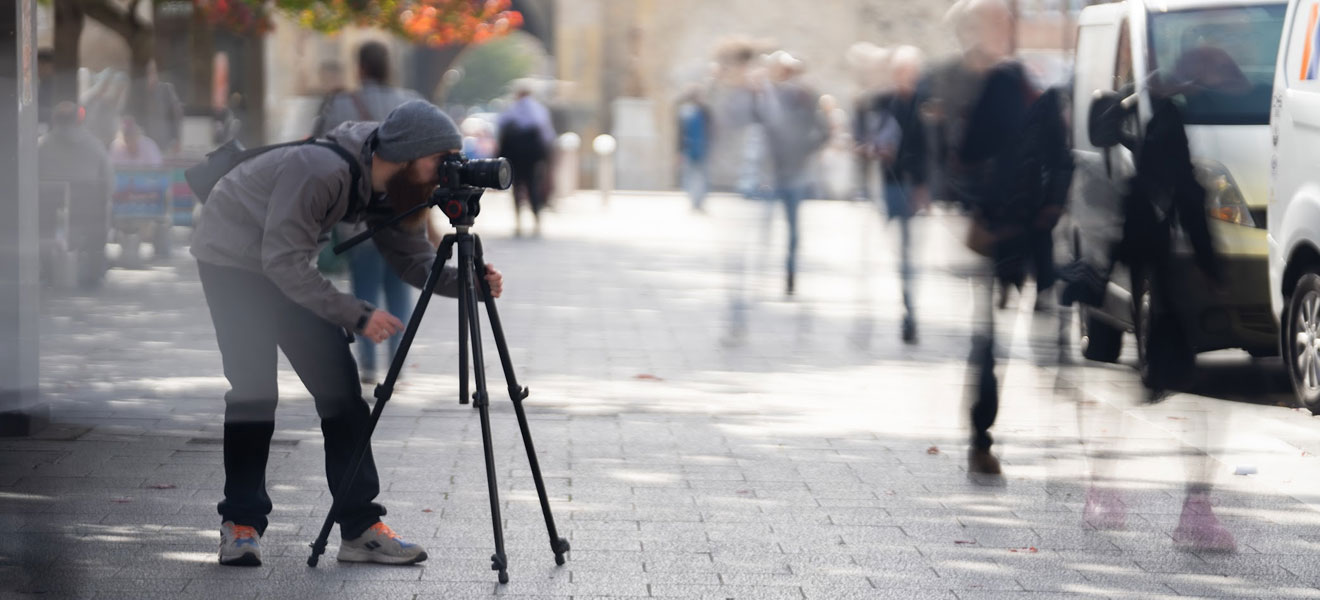 A man using a high-end camera. A time lapse of people walk past.