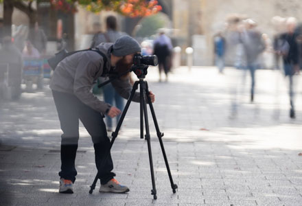 A man using a high-end camera. A time lapse of people walk past.