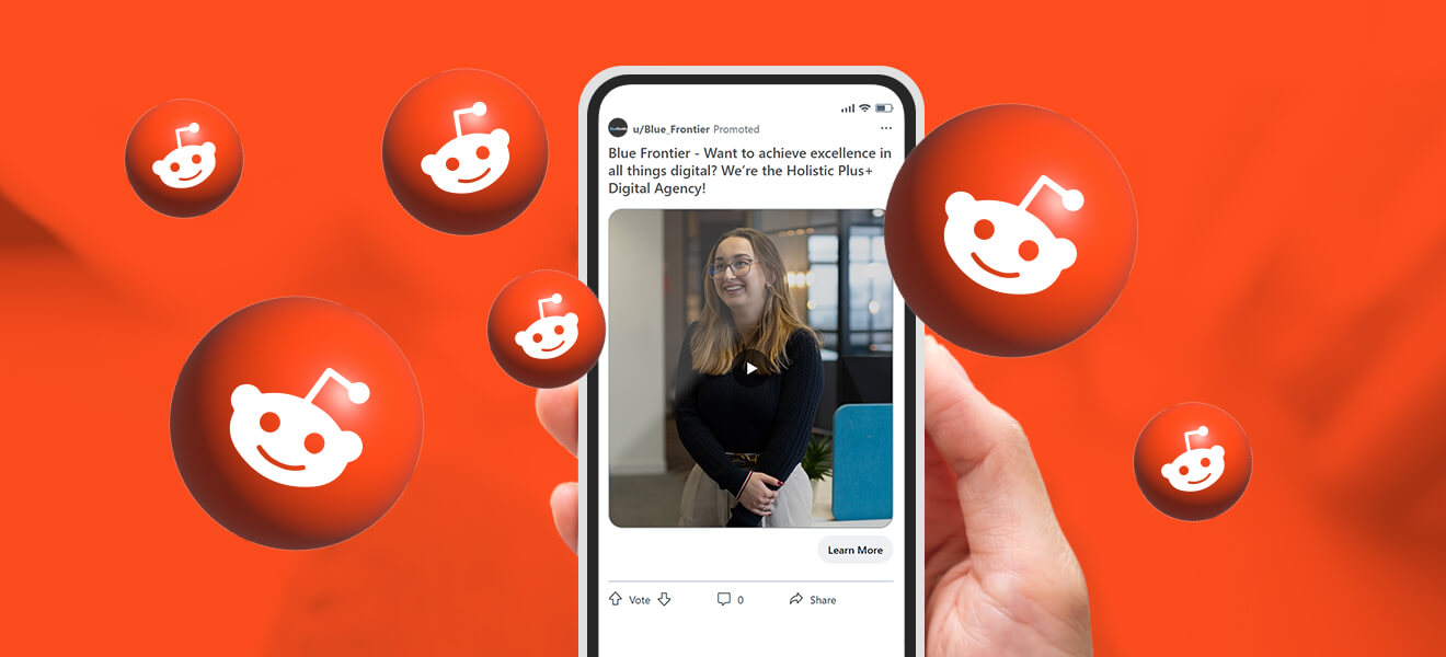 a hand holding up a smart phone with a Reddit advertisement featured on the screen against a bright orange backdrop