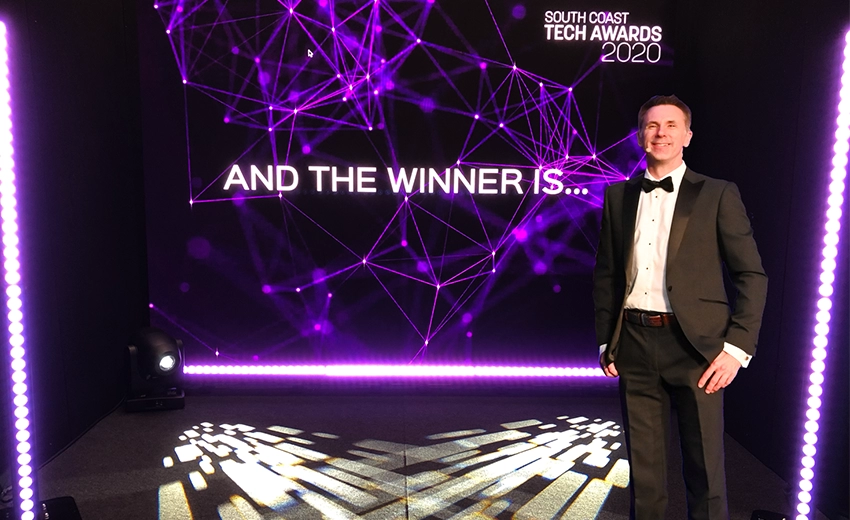 A Tech Award presenter standing in front of a screen displaying 'and the winner is...'