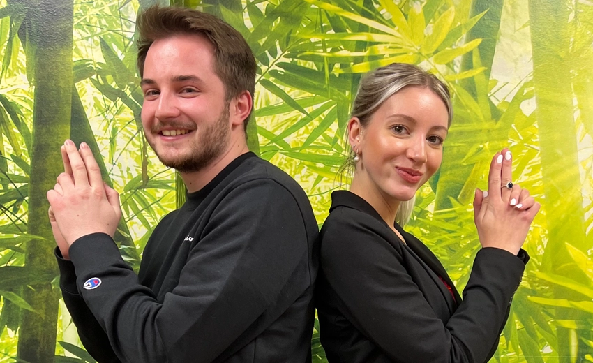 Jake and Tara smiling, standing back-to-back in front of a jungle-themed wallpaper.