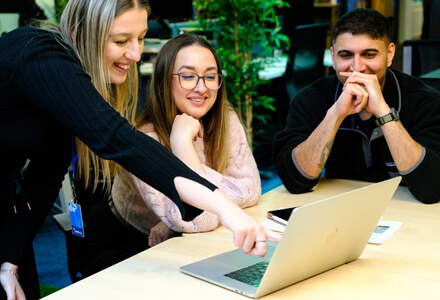 The team sat at a table laughing and talking around a laptop.