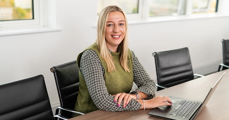 Chloe sitting at the Southampton boardroom table with her laptop and smiling at the camera