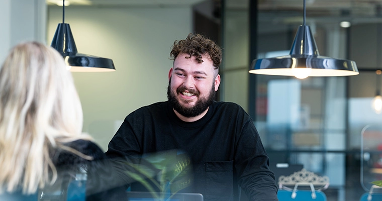 Dan smiling at the Southampton office team collaboration table with Social and Content team leader, Charlotte