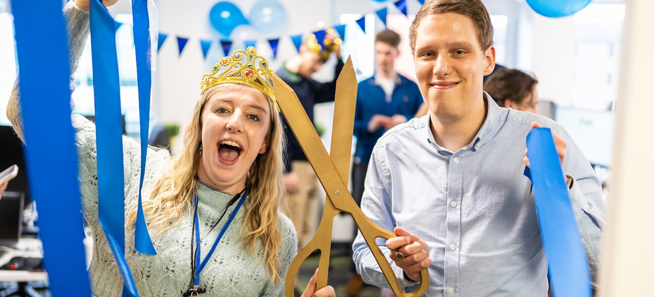 The team celebrating with blue ribbon cutting, bunting and balloons.