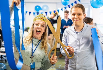 The team celebrating with blue ribbon cutting, bunting and balloons.