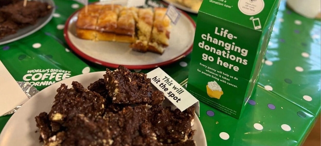 Macmillan donation box next to plates of sweet treats.