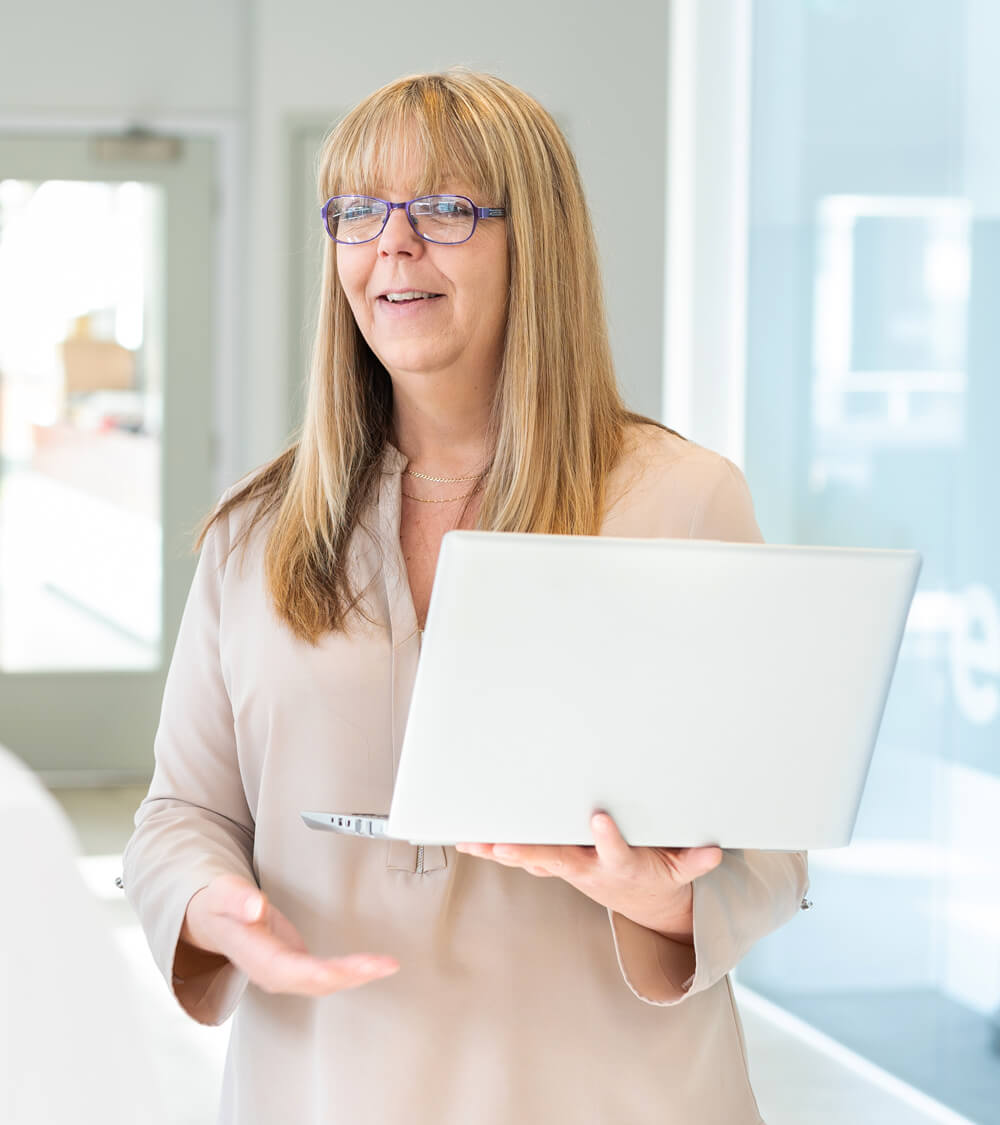 a cyber security consultant holding a laptop and speaking with a client in a bright meeting room