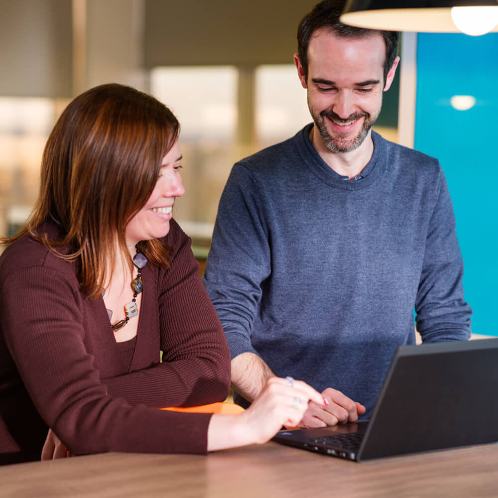 two coworkers working together on a laptop in a modern open-plan meeting space